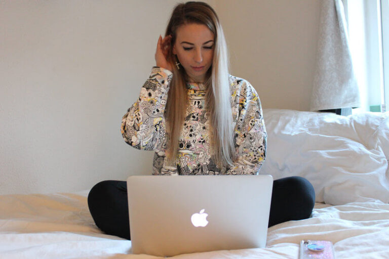 Kvinde der sidder i sin seng med sin MacBook foran sig